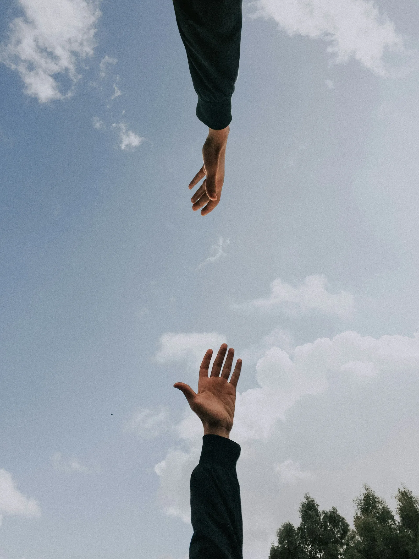 A hand reaching out to another one, against the sky